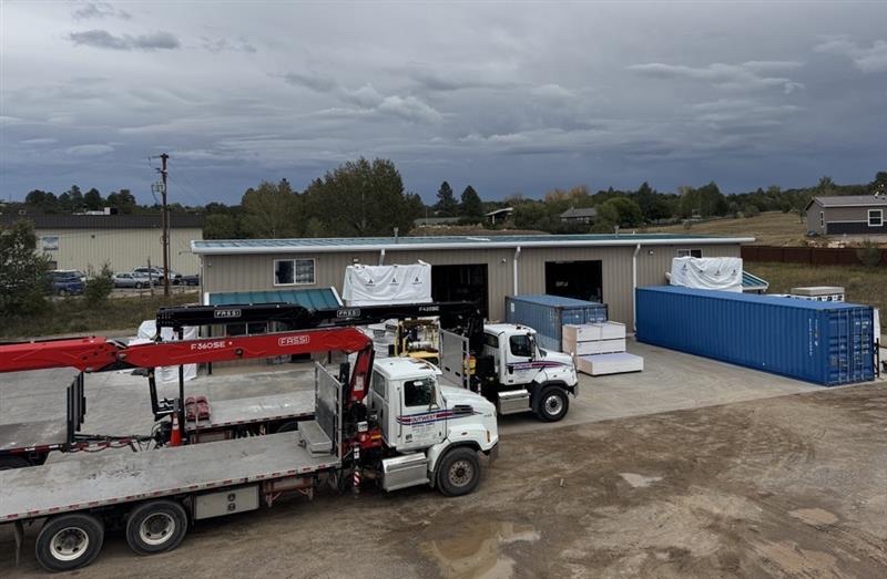 Outwest boom trucks and stocked materials at the Durango yard beneath a cloudy sky