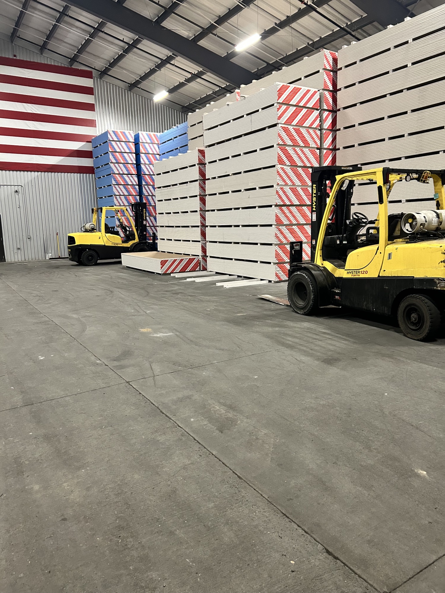 Stacks of drywall and two forklifts inside a warehouse