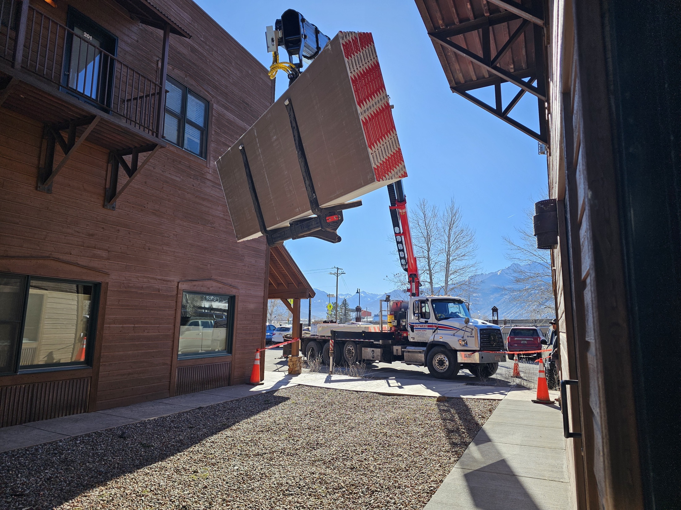 A boom truck lifts a bundle of drywall between two buildings